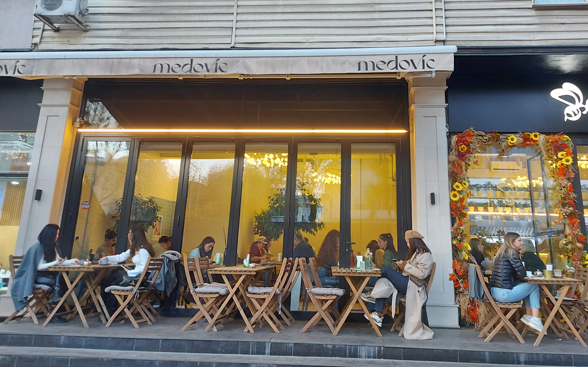 Two people dressed in warm clothes walk by a cafe with flags.