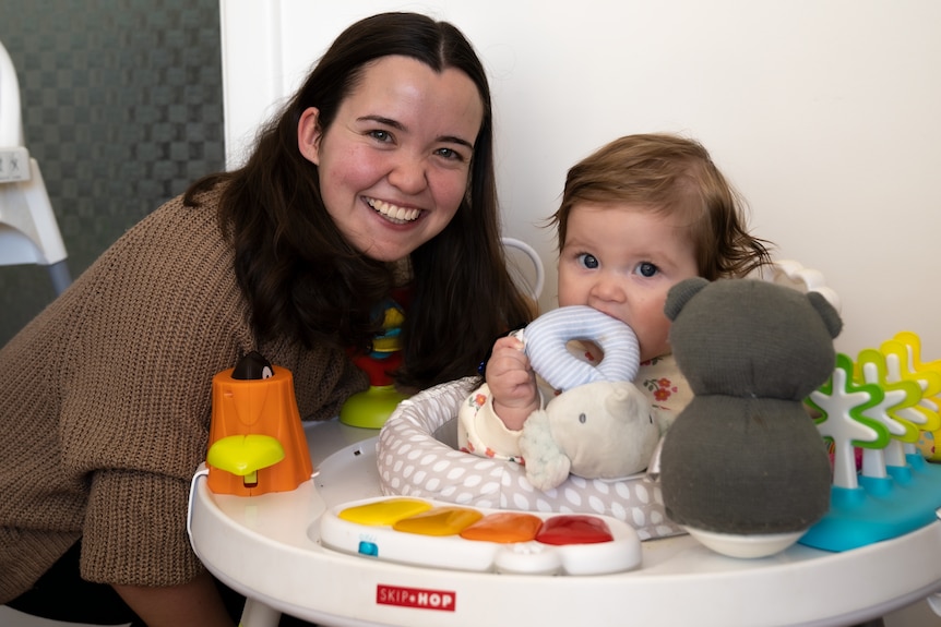 A smiling woman next to a baby in a bouncer