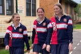 Three teenage girls in school jumpers laugh as they walk through a schoolyard.