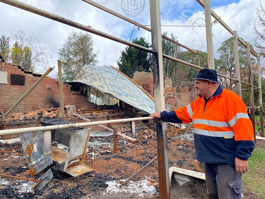 A man leaning on a steel frame looking at a pile of bricks and steel that was his house before it was hit by bushfire.