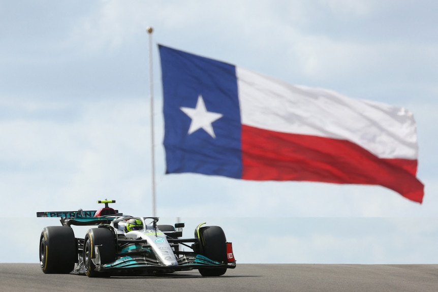 Lewis Hamilton drives past a large flag of Texas.