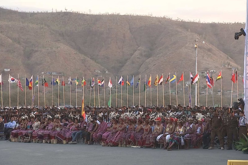 A row of dignitaries in traditional attire sit at the front of a crowd