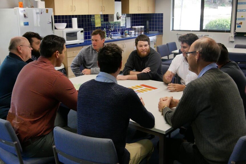 Male teachers sit around a table in the staffroom at Melville Primary School.