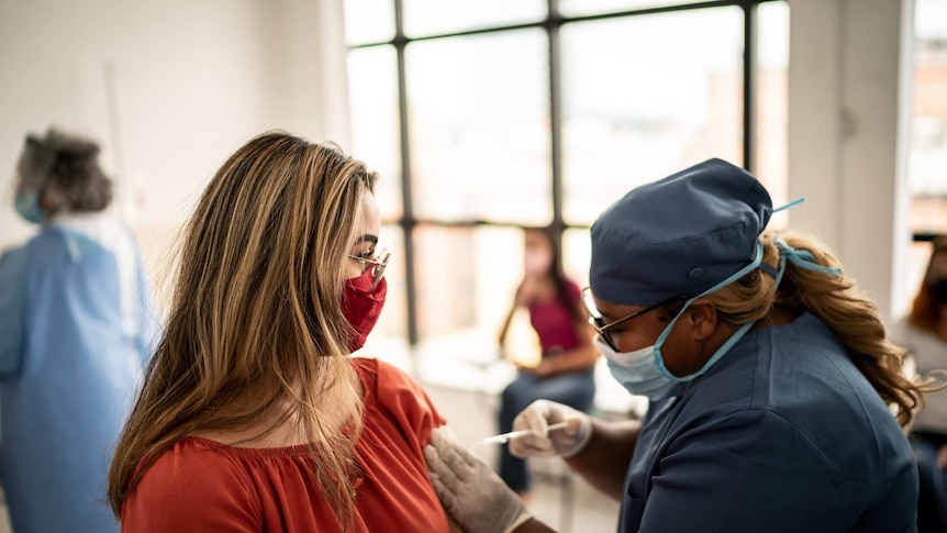 young woman wearing face mask receiving vaccination from nurse