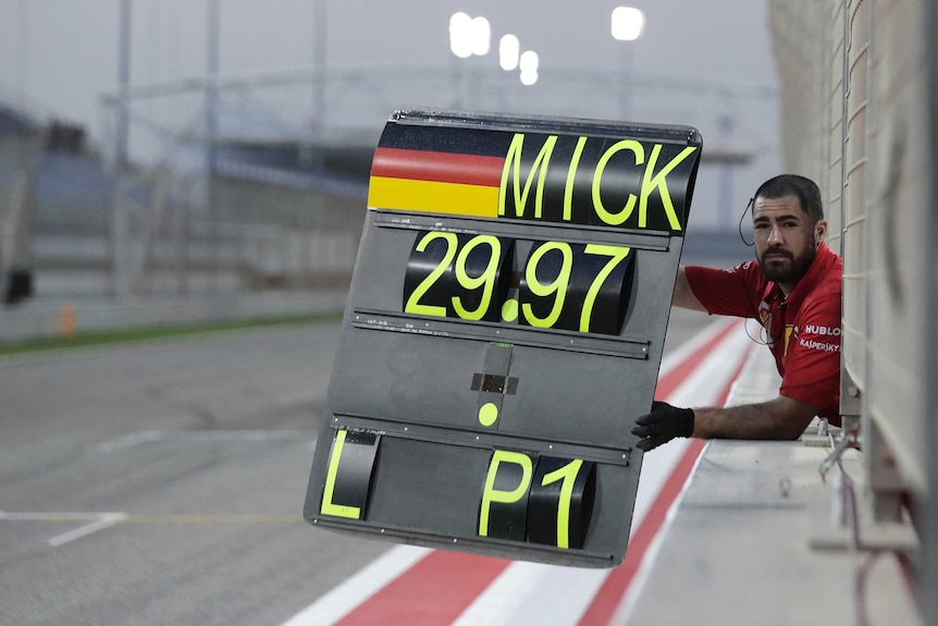 A Ferrari F1 crewman holds a board saying "Mick, 29.97, L - P1" at the Bahrain International Circuit.