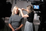 Danielle Laidley sits in a studio, a makeup artist is doing touch up as Danielle prepares for the camera.
