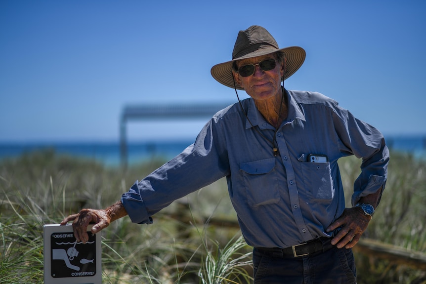 A man in a blue shirt and akubra hat on a coastal strip