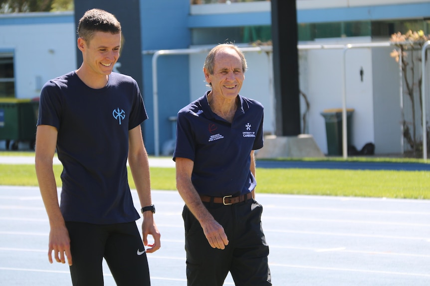 A young man and an older man walk together on an athletics track.