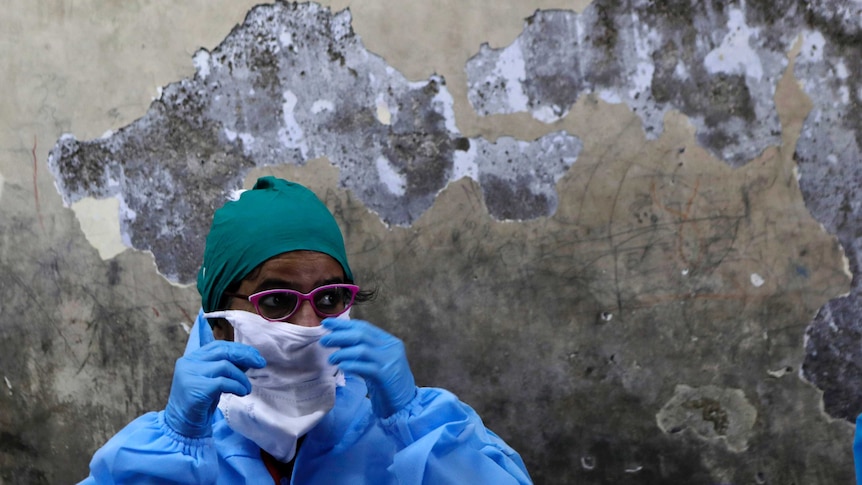 A health worker wearing protective gear raises her hands to her face.