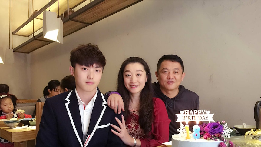 Jeremy Hu sits beside his mother and father at a restaurant with a birthday cake in front of them