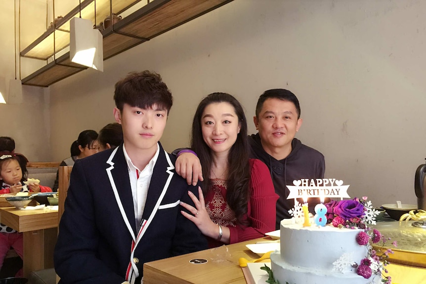 Jeremy Hu sits beside his mother and father at a restaurant with a birthday cake in front of them