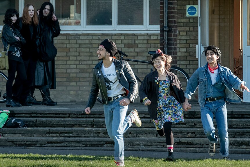 Aaron Phagura, Nell Williams and Viveik Kalra excited run across lawn as a small group of people watch from a distance.