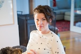 Writer Martha Barnard-Rae, sits at table holding a mug with a serious face