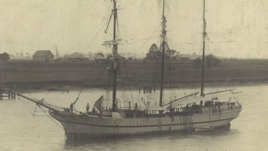 A black and white image of a large three mast sailing boat in a harbour.