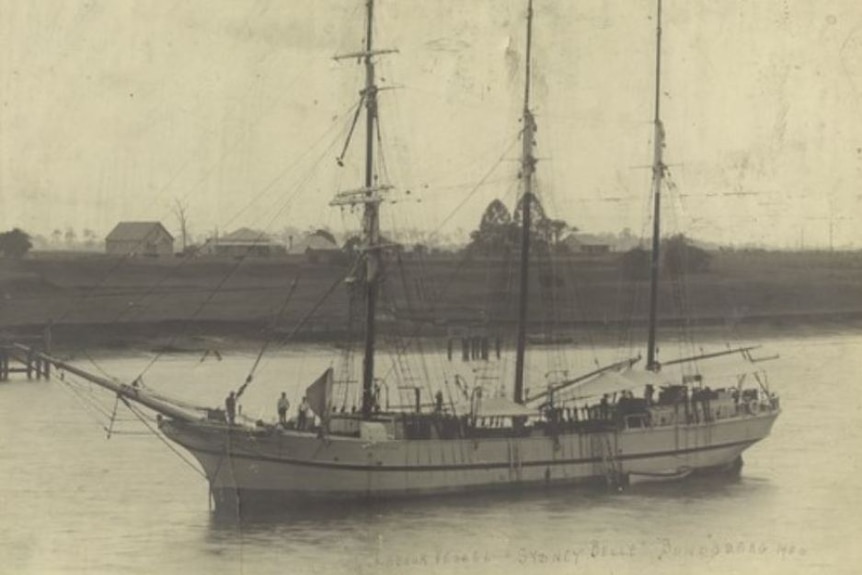 A black and white image of a large three mast sailing boat in a harbour.