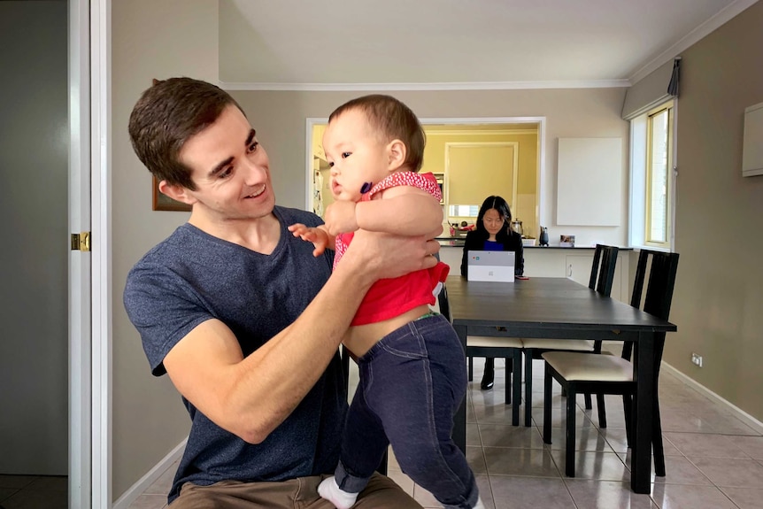 Young dad David Creelman plays with his baby while his wife works.