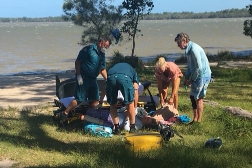 Paramedics and membersof the public surround a stricken woman on the shore of a lake.