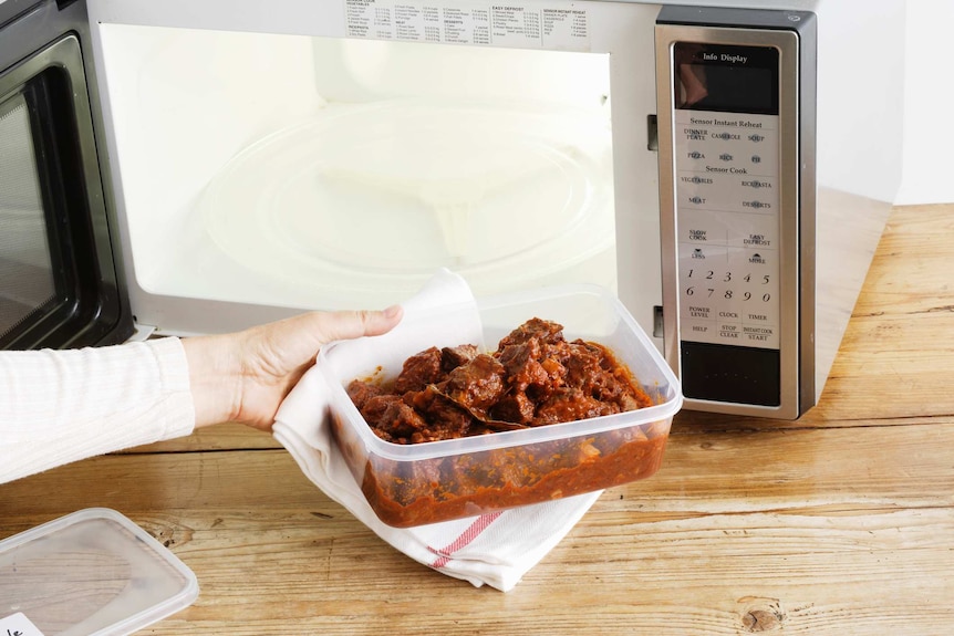 A person puts food in a plastic container into the microwave