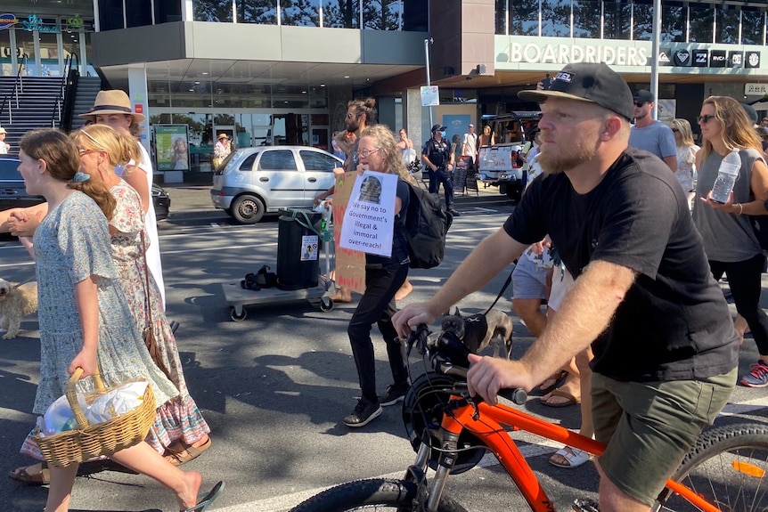 People on bikes, or holding baskets and signs walk along a street.