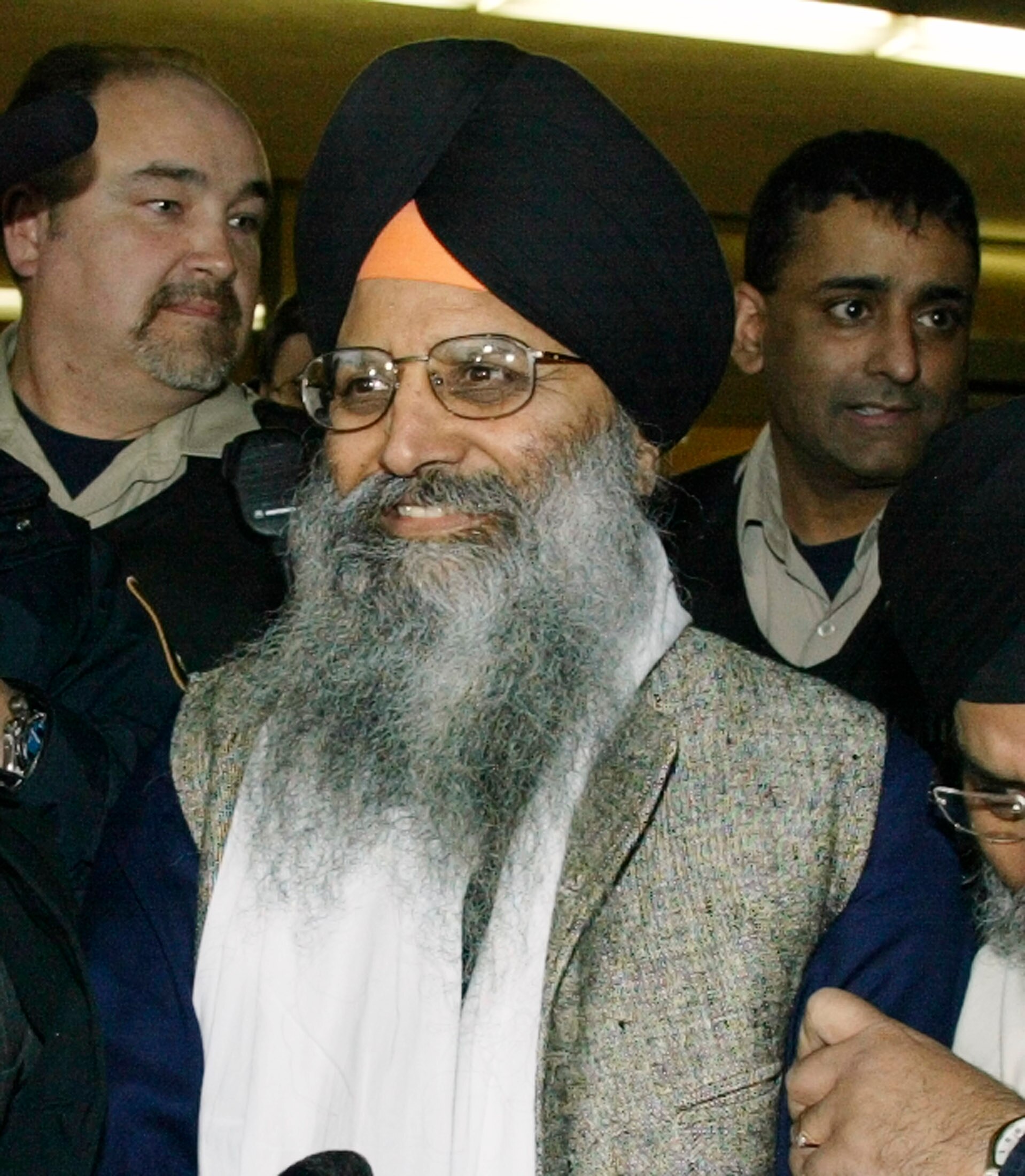 Ripudaman Singh Malik is pictured smiling as he walks from a court with a group of people behind him.