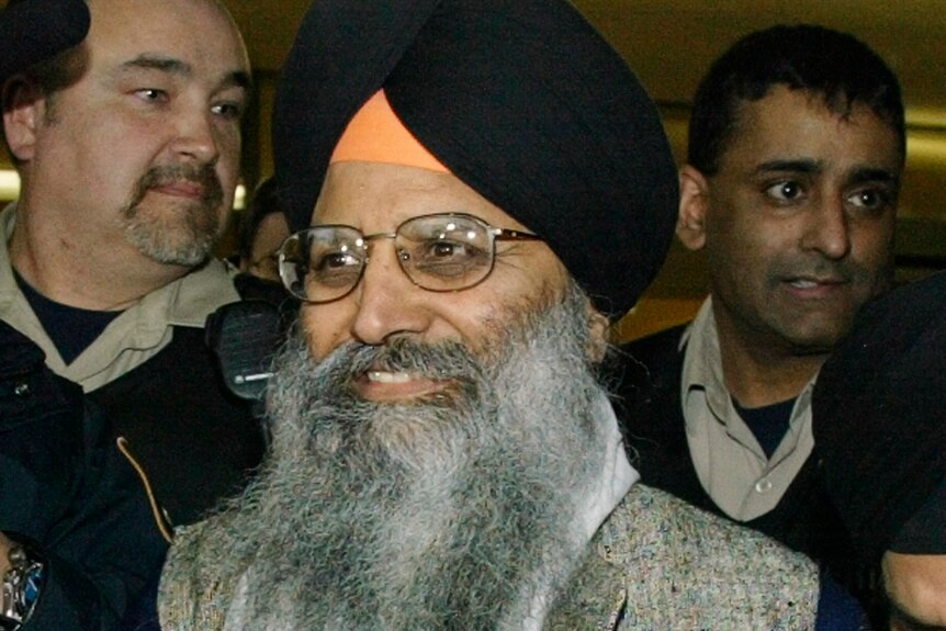 Ripudaman Singh Malik est photographié en train de sourire alors qu'il sort d'un tribunal avec un groupe de personnes derrière lui.