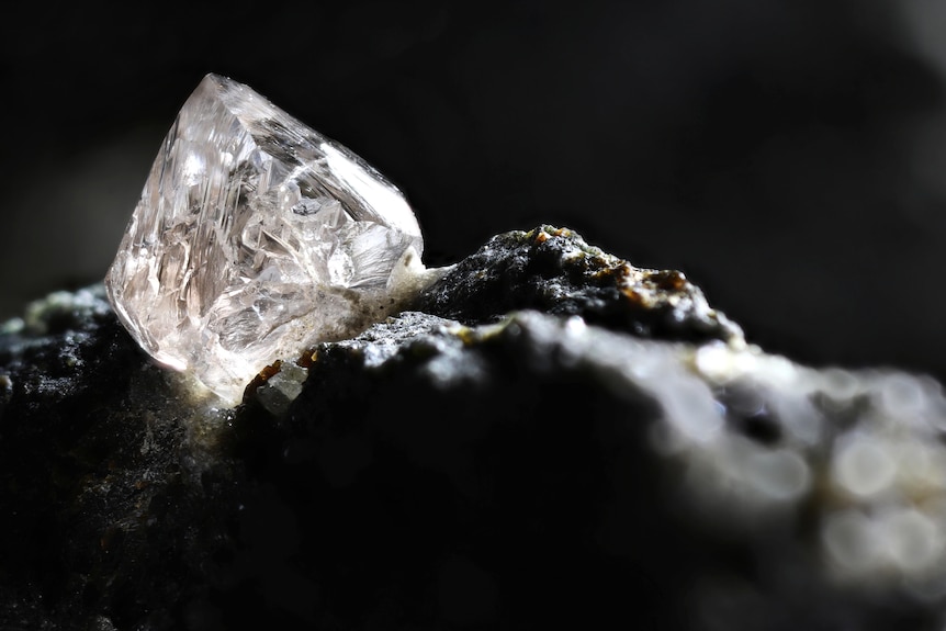 A photo of a sparkling diamond on black rock.