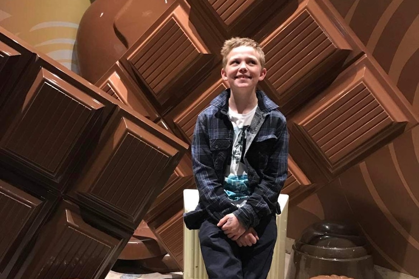 A smiling young boy with fair hair sits among giant plastic blocks of chocolate.