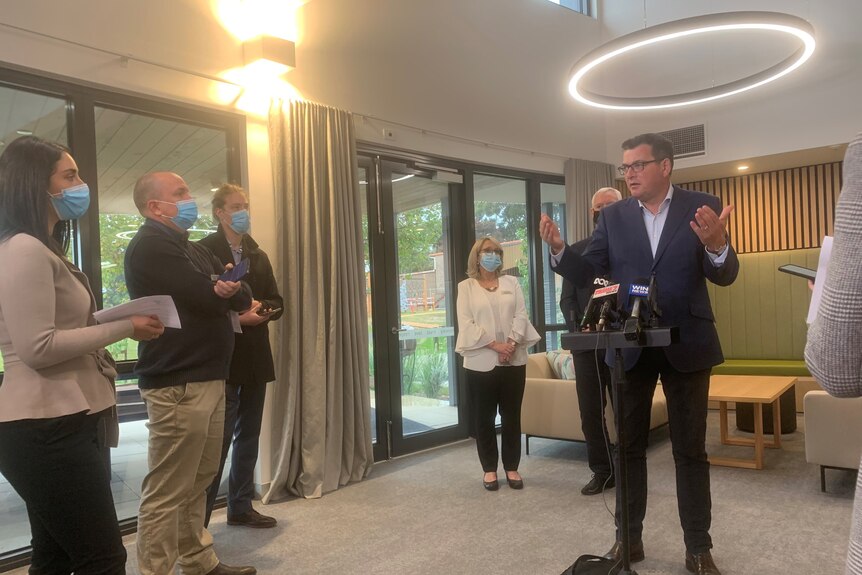 A dark-haired man in a dark suit – Victorian Premier Daniel Andrews – addresses the media in a foyer.