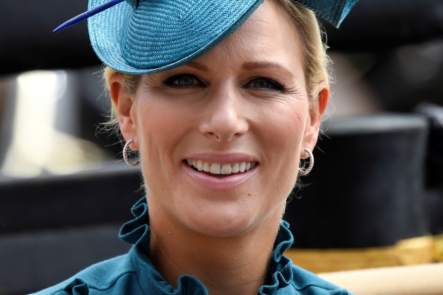 Zara Tindall is smiling and wearing a bright teal hat.