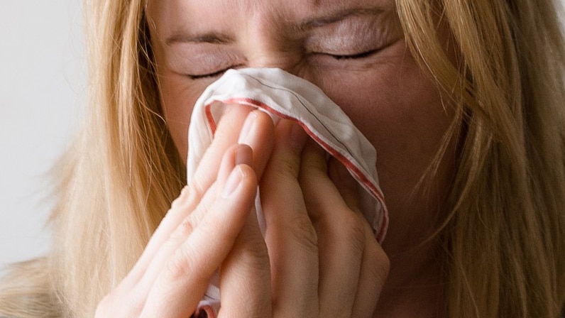 Woman with respiratory illness, blowing her nose into handkerchief.