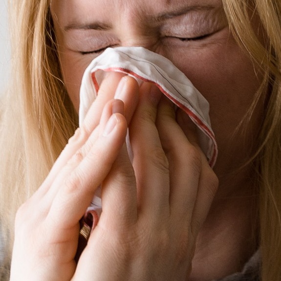 Woman with respiratory illness, blowing her nose into handkerchief.