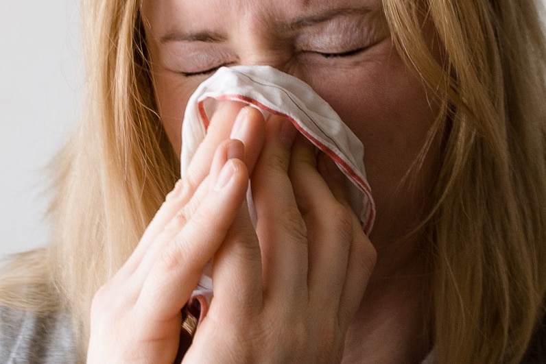 Woman with respiratory illness, blowing her nose into handkerchief.