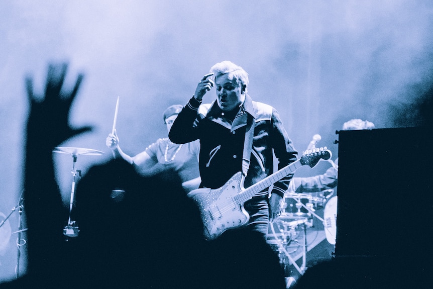 black and white photo of jack white on stage holding his finger up to his temple and holding a guitar