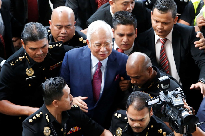 Najib Razak is surrounded by police and others as he walks towards court.