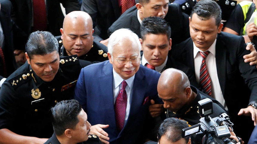 Najib Razak is surrounded by police and others as he walks towards court.