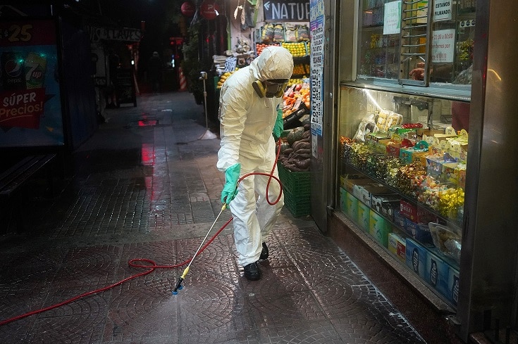 A municipal worker wearing personal protective equipment (PPE) disinfects a bus stop.