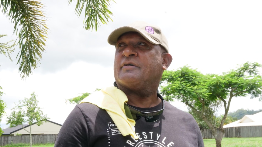 Man wearing a black t-shirt and beige cap, looking at the sky.