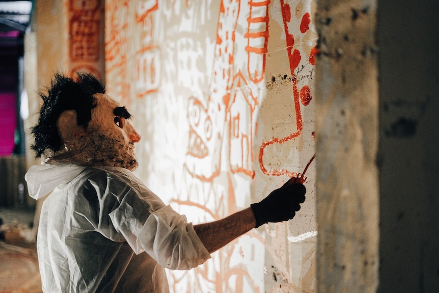 Un homme portant un masque peint une peinture murale sur le mur