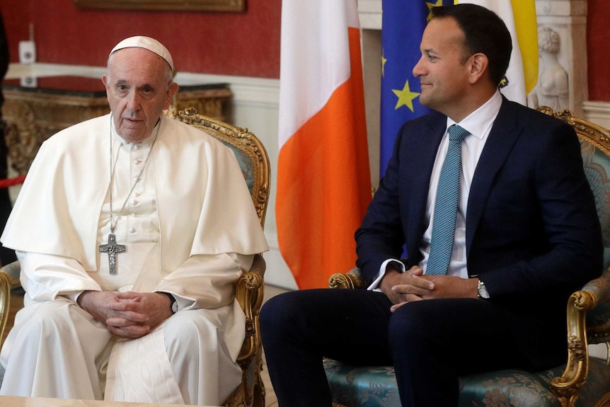 Pope Francis (left) sits on a chair next to Leo Varadkar (right) who looks at him.
