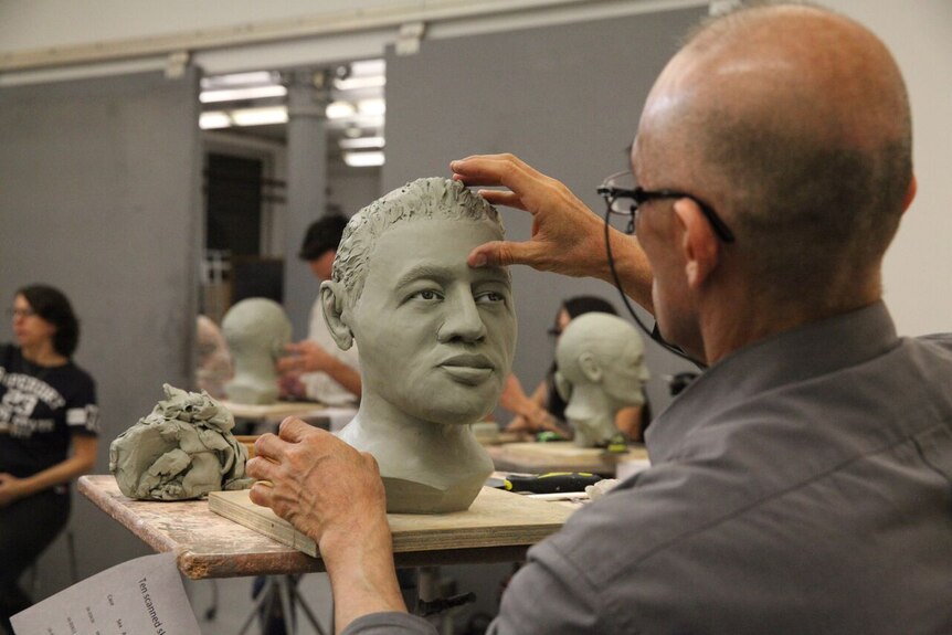A student works on a sculpture of a human face.