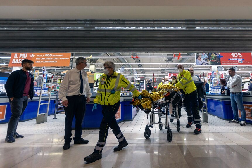 Emergency personnel wheel an injured person on a stretcher out of a supermarket.