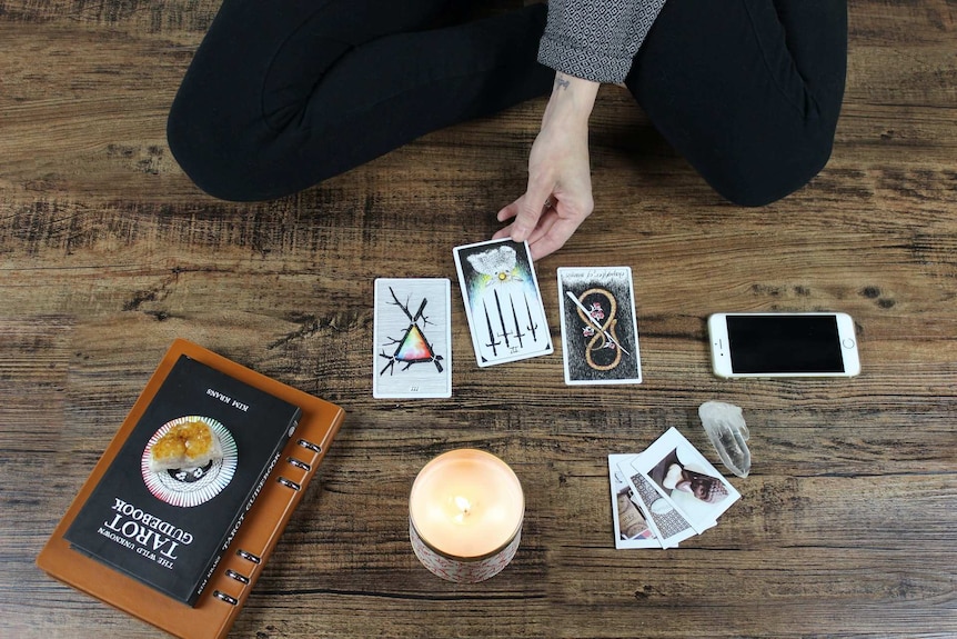 A woman sits on the floor arranging tarot cards around a candle