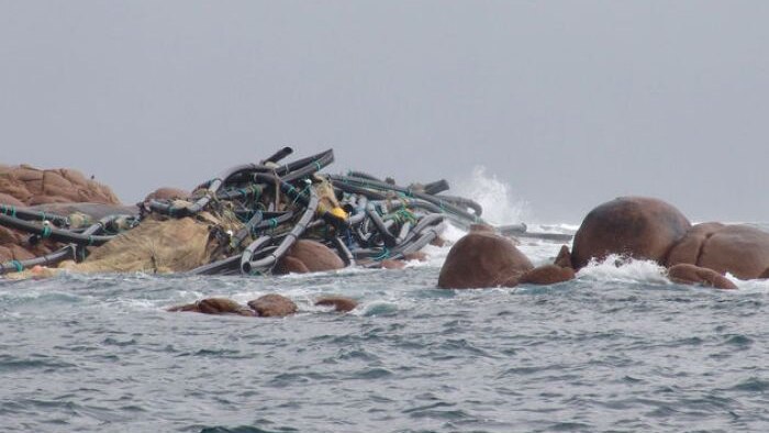 A large pile of debris lays on top of rocks out in the ocean