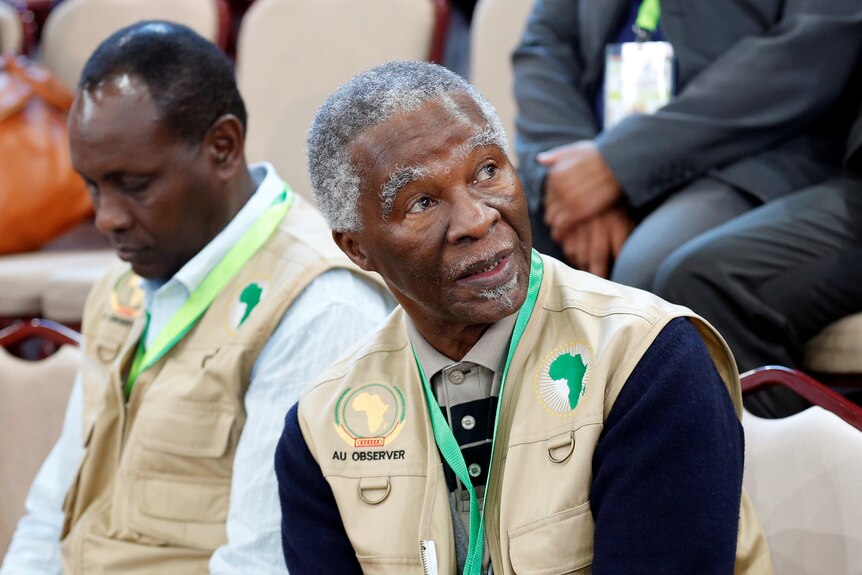 An older African man wearing a vest labelled "observer" sits in a voting tally centre.