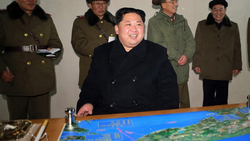North Korean leader Kim Jong-un sits at desk with map on it and generals standing behind him