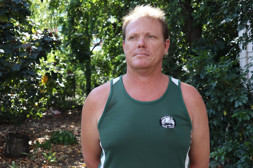 a man wearing a green singlet in front of dense bushland
