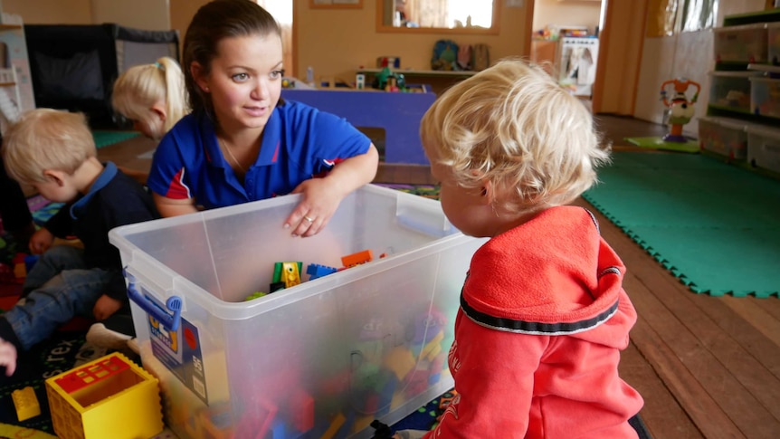 A female childcare worker plays with children and toys in a centre.