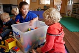A female childcare worker plays with children and toys in a centre.