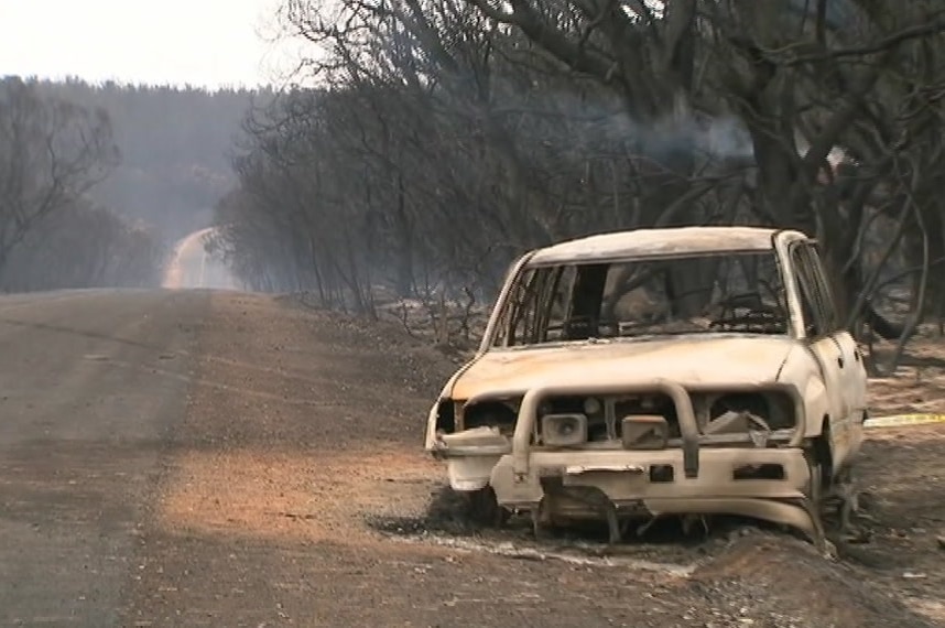 A burnt four-wheel drive on a road with black trees