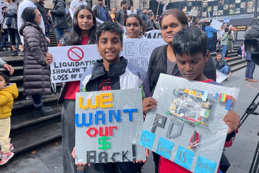 Two boys hold signs at a protest about collapsed home builder Porter Davis at Victoria's parliament.